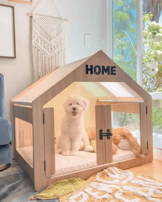 A fluffy white dog sitting happily inside a modern, house-shaped wooden indoor dog crate with clear acrylic panels in a bright, tranquil living room.